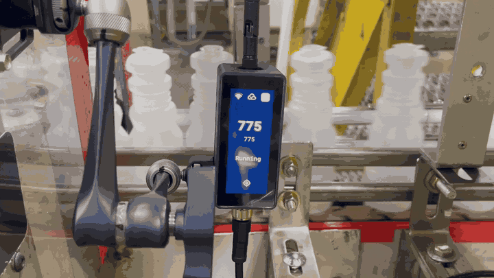 Bottles moving along a conveyor past a bracket-mounted BeamTracker, whose screen shows the part count rising from 775 and a green Running status